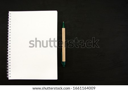 white notebook and pen on a black table. Space for text.