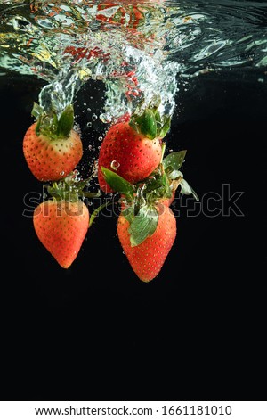 Red fresh strawberries are thrown into the water, under the water. Splash of water. Red berries on a black background.