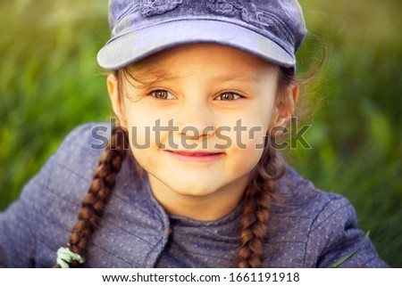 Happy smiling kid girl looking on the glass in blue clothing on summer green background. Closeup portrait
