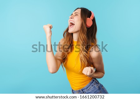 Portrait of beautiful joyous woman wearing headphones listening to music isolated over blue background in studio