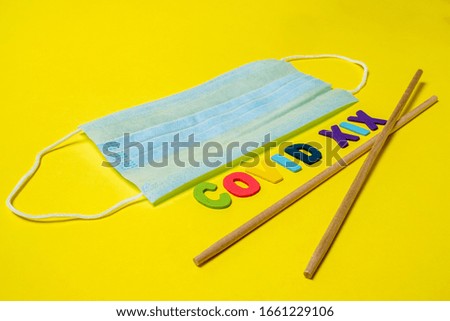Blue medical mask on a yellow background and Asian chopsticks in the shape of the letter V. The inscription indicates the virus. Safe delivery of disinfected food during quarantine of the coronavirus.