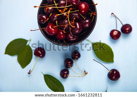 Ripe sweet cherry in a black bowl on a wooden table, top view. Delicious berries.
