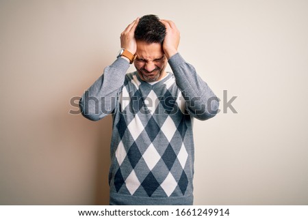 Young handsome man wearing casual sweater standing over isolated white background suffering from headache desperate and stressed because pain and migraine. Hands on head.