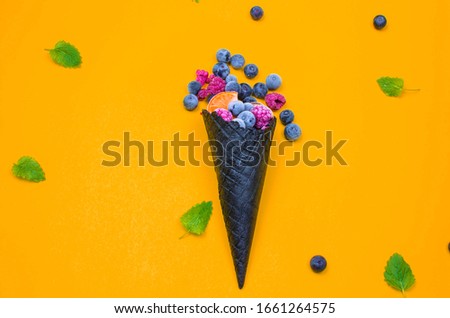 Blueberry Ice Cream. on a yellow background. frozen Raspberry and orange and blueberries from the horn. ice cream with copy space. 