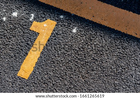 Number 1 on asphalt parking lot with yellow lot line.