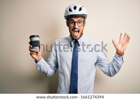 Young businessman wearing glasses and bike helmet drinking cup of coffee very happy and excited, winner expression celebrating victory screaming with big smile and raised hands