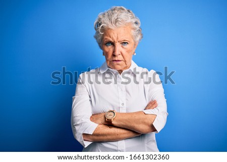 Senior beautiful woman wearing elegant shirt standing over isolated blue background skeptic and nervous, disapproving expression on face with crossed arms. Negative person. Royalty-Free Stock Photo #1661302360