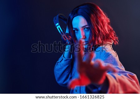 Portrait of young girl that listening to music in headphones in red and blue neon in studio.