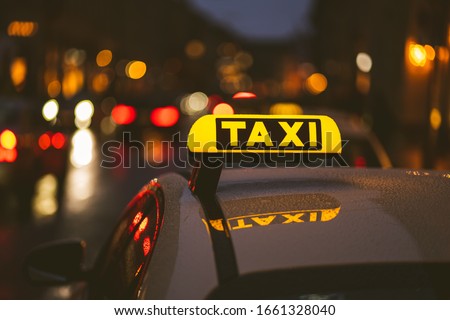 Illuminated taxi sign on top of a car. City lights with neon color in the background. Rainy urban night scene. Royalty-Free Stock Photo #1661328040