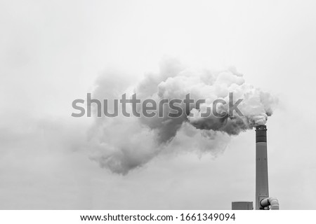 Thick and heavy smoke coming out of a huge and high chemical factory chimney under a misty and rainy sky Royalty-Free Stock Photo #1661349094