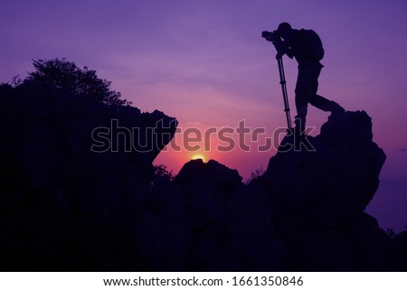 Photographer climbing on the top of the mountain to take a picture at sunset.