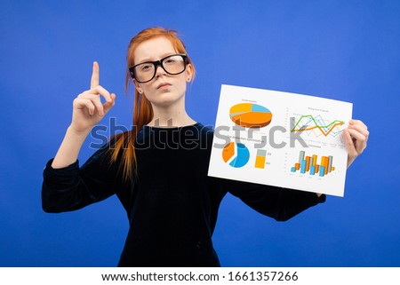 smart teenager girl in glasses and a black dress shows statistics on diagrams on a blue background