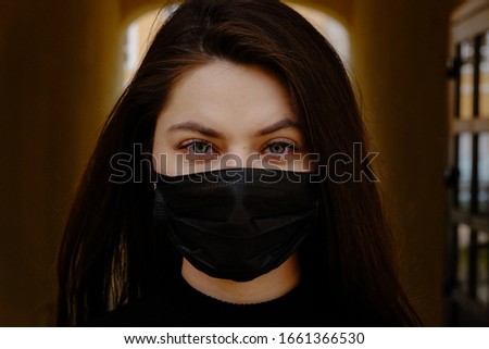 Girl, young woman in protective sterile medical mask on her face looking at camera outdoors close up.  Corona virus pandemic. Beautiful brunette haired girl with medical mask.