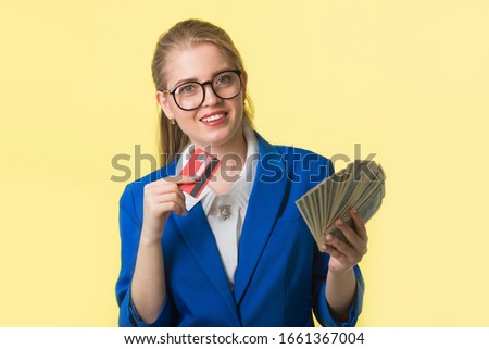 beautiful young woman in a blue jacket on a yellow background with dollars and a credit card in hands