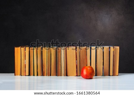 Back to school, pile of books and red apple with empty black school board background, education concept