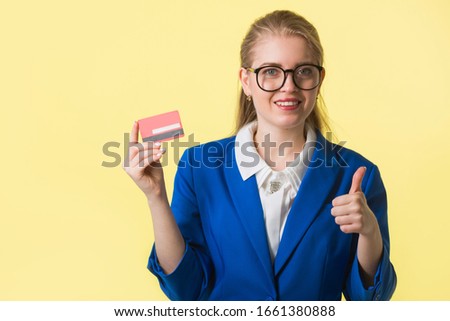 beautiful young woman in a blue jacket on a yellow background with a credit card in hand