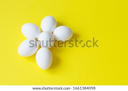 Six white eggs lie on a bright yellow background in the shape of a Daisy. Good morning concept