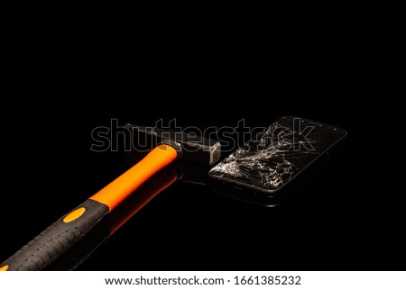 The smartphone is broken by a hammer on a black background.