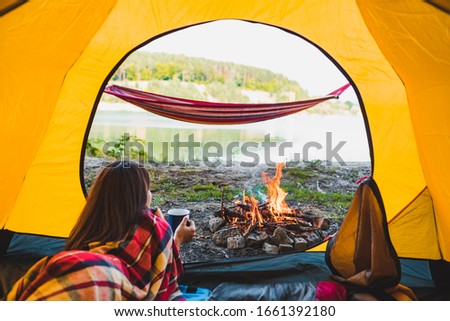woman laying in yellow tent looking at bonfire
