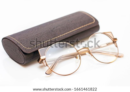 modern fashionable womens gold glasses for sight and a leather case on a light background.