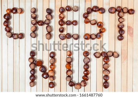 Word chestnut is laid out with ripe brown nuts chestnuts on light wooden background close up for your design. Flat lay.