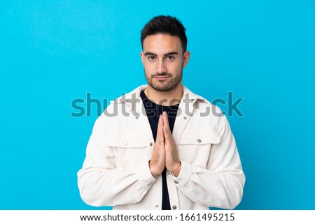 Young handsome man over isolated blue background pleading