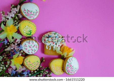 Flat lay Easter treats gingerbread cookies in the form of Easter cake, Easter eggs and rabbits decorated with glaze with spring flowers on a pink background with place for text