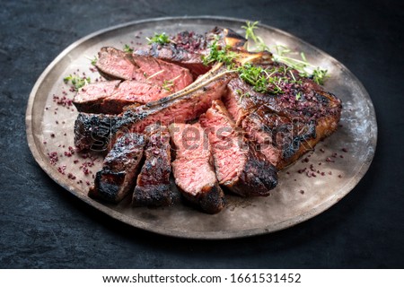 Barbecue dry aged wagyu porterhouse beef steak sliced with large fillet piece with herbs and red salt as closeup on a modern design rustic plate  Royalty-Free Stock Photo #1661531452
