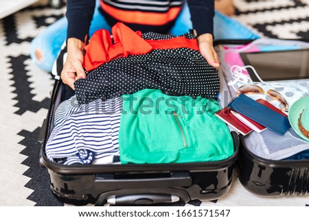Beautiful young woman packing her stuff into a big suitcase. Traveling preparation concept. 