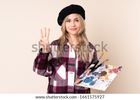 Teenager artist girl holding a palette isolated on blue background happy and counting three with fingers