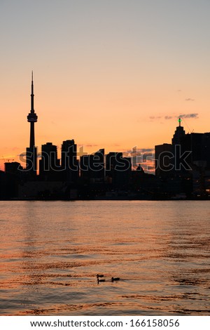 Toronto city skyline silhouette at sunset over lake with urban skyscrapers.