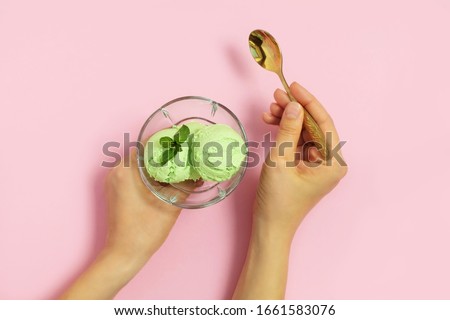 Woman hands holding glass cup with homemade avocado ice cream and golden spoon on light pink background. Top view, flat lay Royalty-Free Stock Photo #1661583076