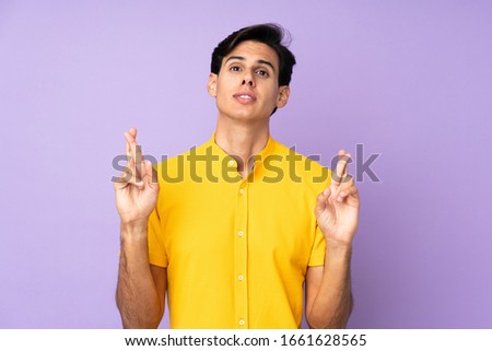 Man over isolated purple background with fingers crossing and wishing the best