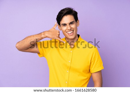 Man over isolated purple background making phone gesture. Call me back sign