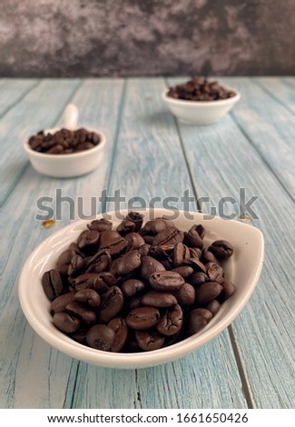 Roasted coffee on the white bowl  over the wooden background with grains and empty space.

