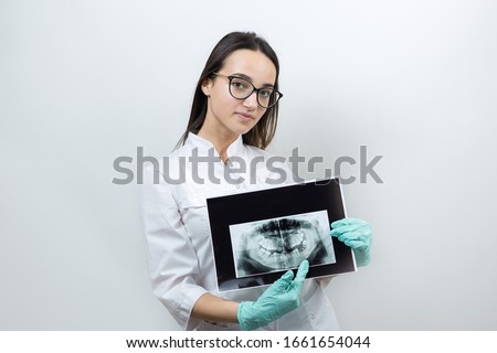 Girl dentist in a white coat holds a snapshot of the patient's teeth.