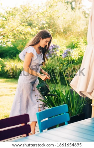 Pretty young woman watering plants in summer garden