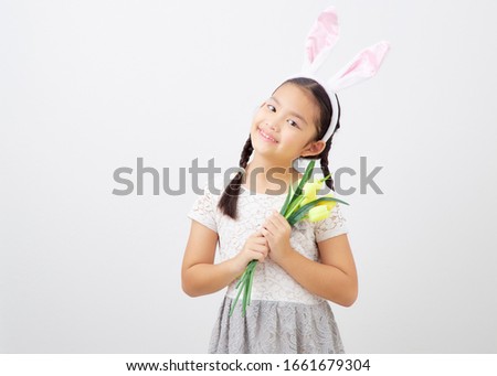 Asian little girl with pink ears bunny holding a bouquet of yellow tulips on white background. Concept of holidays