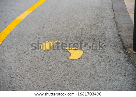 Walkway lane with yellow footsteps signs near yellow line on pavement road in public park