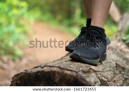 Close-up action at trail or trekking runner's foot during standing on timber, it also have pathway in the forest as background. Sport and adventure recreation concept photo.