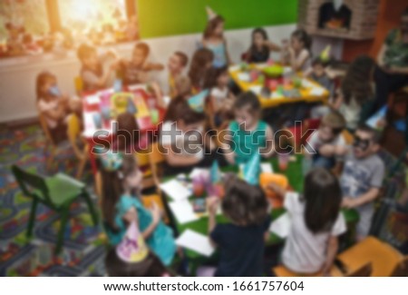 Blurred image for background usage. Kids at birthday party in a play room, sitting on little chairs.
