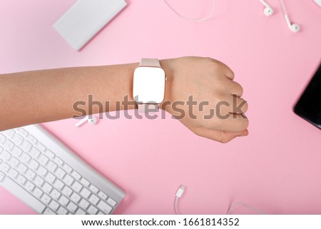 Female hand with a pink smart watch. Mockup of smart woman gadgets on the pink background. Woman using smart watch, modern city lifestyle