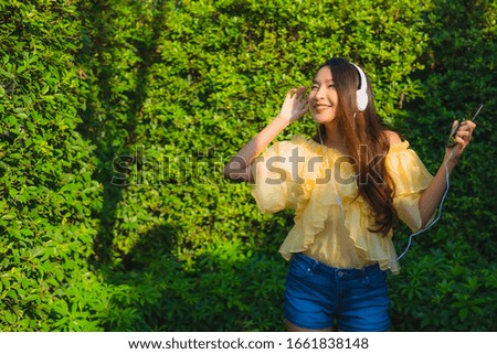Young asian woman using smart mobile phone with headphone for listen music around outdoor garden nature view