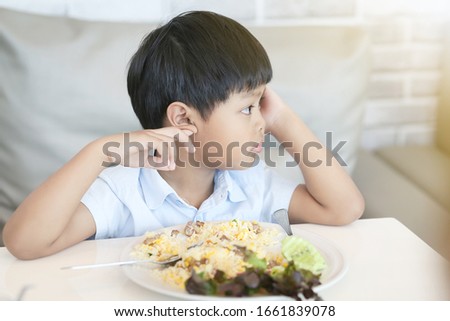 An Asian boy make boring face when he eat vegetable. Unhappy, disgusted, unlike food. 