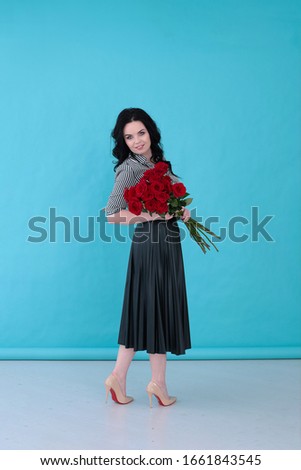 Beautiful young woman with a striped blouse and pleated skirt on a bright turquoise background