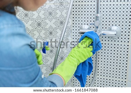 Cleaning bathroom, woman in gloves with rag and detergent, washing and polishing shower, glass, faucet, tiled wall