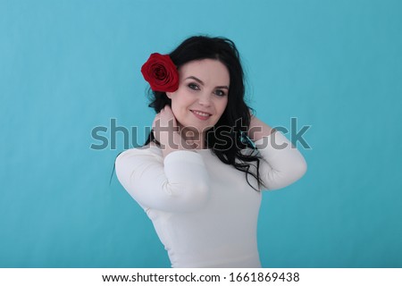 Woman of thirty years with curly black hair and a rose in a white dress on a juicy turquoise background