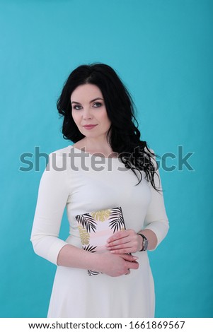 Woman of thirty years with curly black hair and a rose in a white dress on a juicy turquoise background