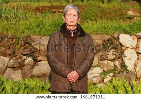 The old man standing on the ridge of the field looking at the camera Royalty-Free Stock Photo #1661871211