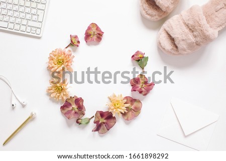 Flat lay round frame border with copy space made of flower buds on bloggers desk. Top view floral concept, feminine workspace.